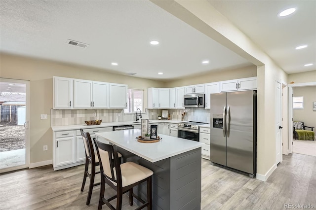 kitchen with stainless steel appliances, white cabinets, visible vents, and backsplash