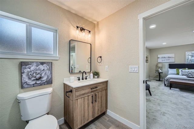 bathroom with toilet, a textured wall, vanity, and baseboards