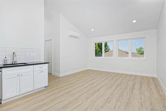 kitchen with an AC wall unit, light wood-type flooring, white cabinetry, sink, and vaulted ceiling