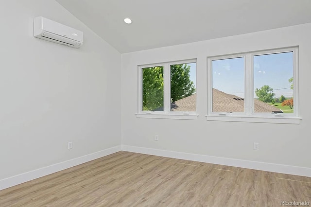 spare room featuring vaulted ceiling, an AC wall unit, and light hardwood / wood-style flooring