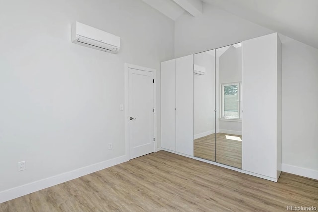 unfurnished bedroom with light hardwood / wood-style floors, a closet, beamed ceiling, and a wall mounted air conditioner