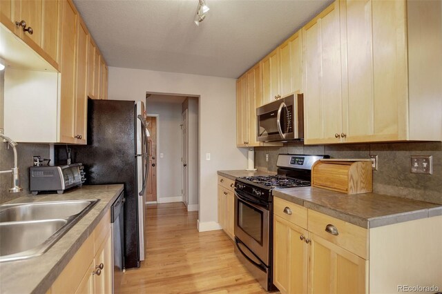 kitchen featuring appliances with stainless steel finishes, tasteful backsplash, light wood-style flooring, and light brown cabinetry