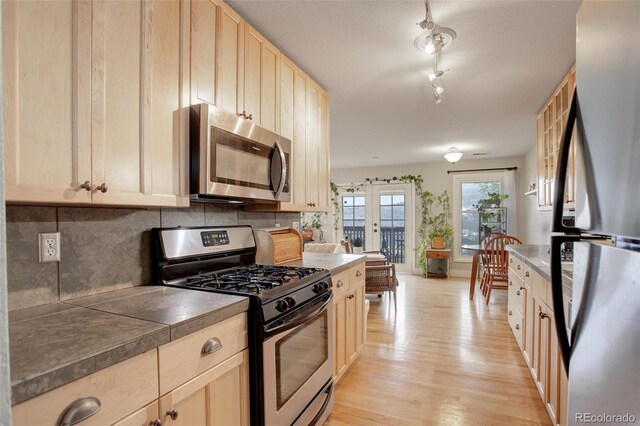 kitchen featuring appliances with stainless steel finishes, light brown cabinetry, light wood-style flooring, and backsplash