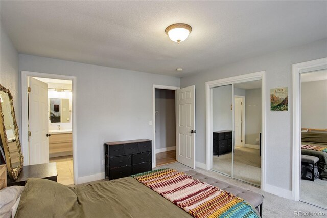 bedroom featuring two closets, baseboards, ensuite bathroom, and light carpet