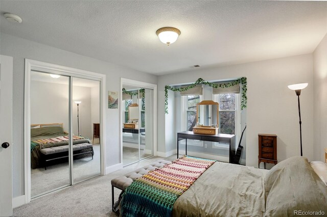 carpeted bedroom featuring two closets, baseboards, and a textured ceiling