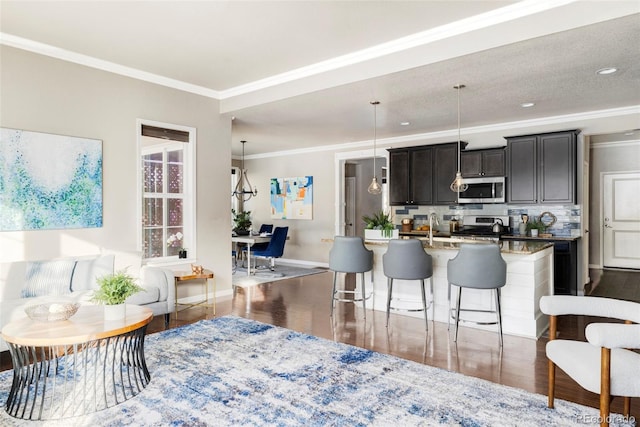 kitchen featuring pendant lighting, a breakfast bar area, a kitchen island with sink, stainless steel appliances, and crown molding