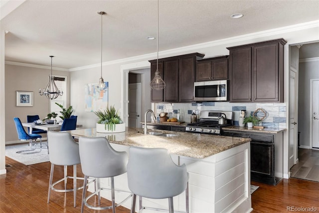 kitchen featuring sink, a kitchen island with sink, hanging light fixtures, dark brown cabinets, and stainless steel appliances