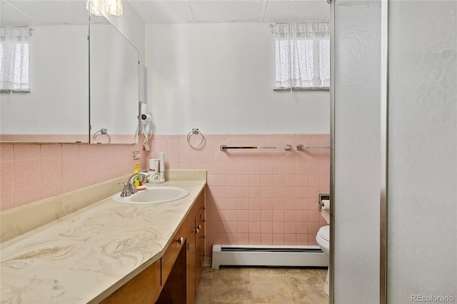 5960 Glencoe St, Commerce City, CO 80022 - bathroom featuring a baseboard radiator, vanity, tile walls, toilet, and healthy amount of natural light