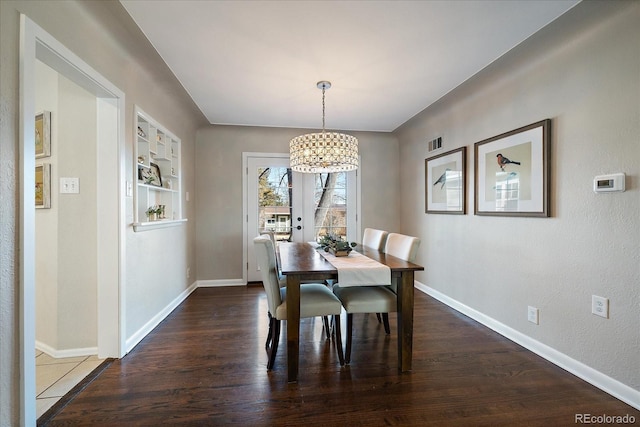 dining area with dark wood-type flooring and an inviting chandelier