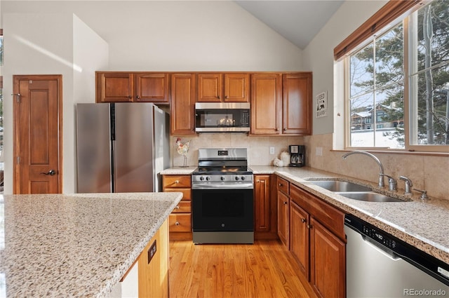 kitchen with sink, stainless steel appliances, lofted ceiling, decorative backsplash, and light wood-type flooring