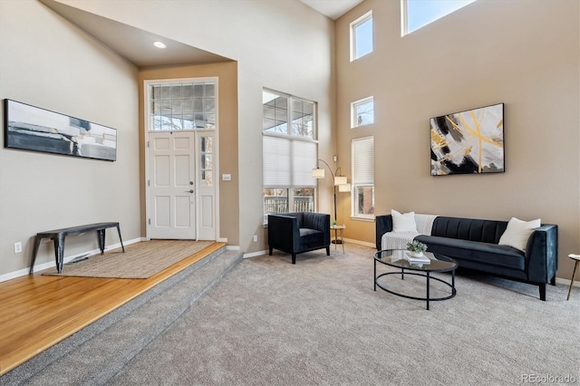 carpeted living room featuring a high ceiling, baseboards, wood finished floors, and recessed lighting