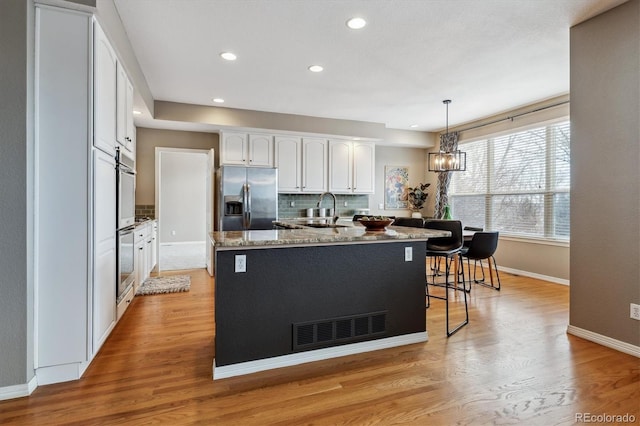 kitchen featuring white cabinets, stainless steel fridge with ice dispenser, a kitchen island with sink, pendant lighting, and a sink