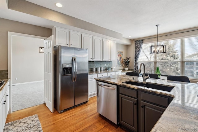 kitchen with light stone counters, stainless steel appliances, a sink, white cabinetry, and hanging light fixtures