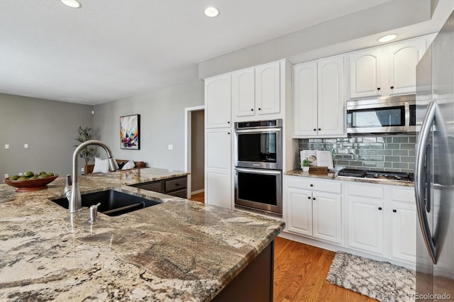 kitchen with light stone counters, stainless steel appliances, white cabinetry, a sink, and light wood-type flooring