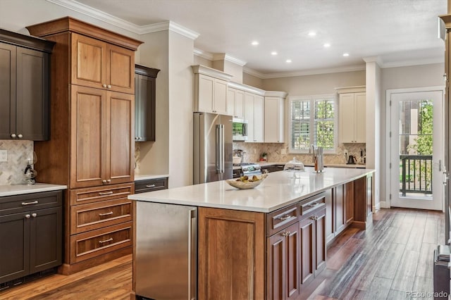 kitchen featuring appliances with stainless steel finishes, tasteful backsplash, crown molding, wood-type flooring, and a center island