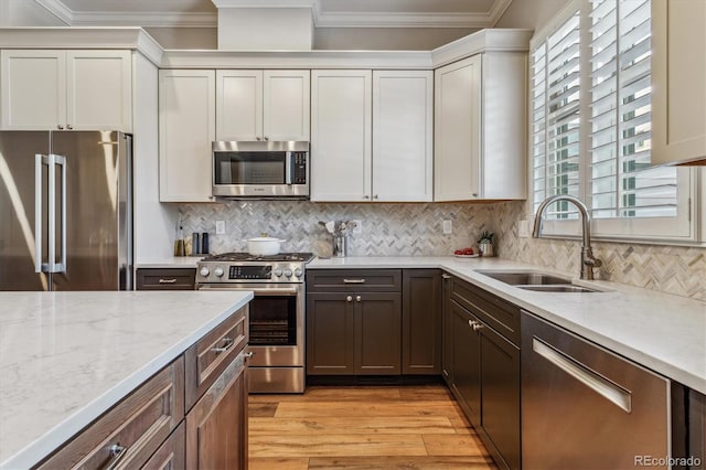 kitchen with high end appliances, sink, crown molding, white cabinets, and light wood-type flooring