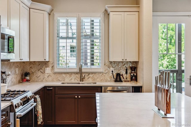 kitchen with light stone countertops, appliances with stainless steel finishes, backsplash, dark brown cabinetry, and sink