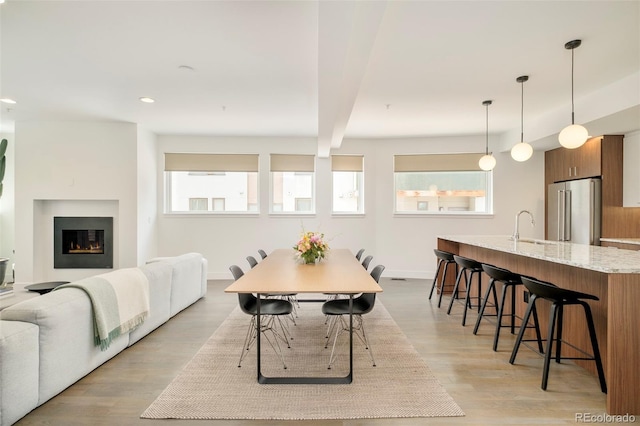 dining room with baseboards, a warm lit fireplace, light wood-style floors, and a healthy amount of sunlight