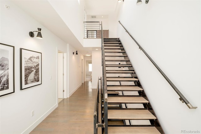 stairway with baseboards, wood finished floors, and a high ceiling