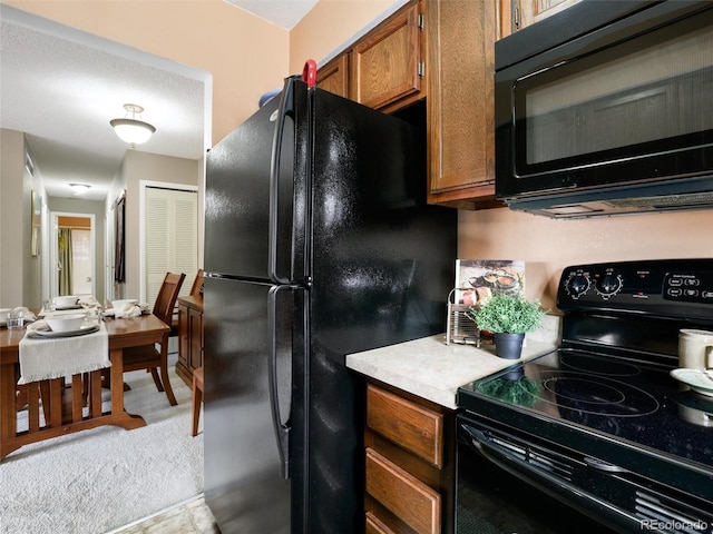 kitchen with black appliances, light countertops, brown cabinets, and light carpet