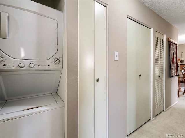 laundry area featuring light colored carpet, stacked washer and dryer, laundry area, and a textured ceiling