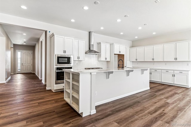 kitchen with white cabinets, stainless steel appliances, a kitchen island with sink, and wall chimney exhaust hood