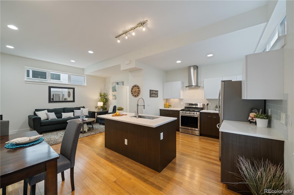 kitchen with sink, wall chimney range hood, white cabinetry, gas stove, and a center island with sink