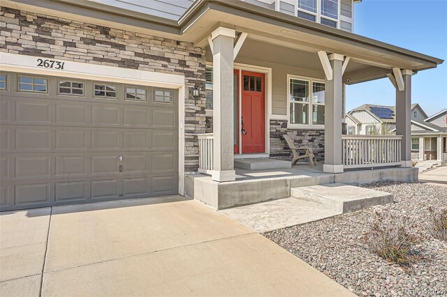 26731 E Hinsdale Pl, Aurora, CO 80016 - entrance to property featuring covered porch, driveway, stone siding, and a garage