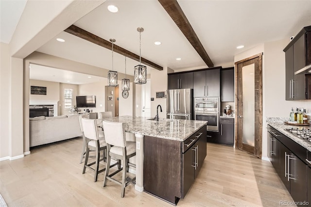 26731 E Hinsdale Pl, Aurora, CO 80016 - kitchen featuring beamed ceiling, an island with sink, a kitchen breakfast bar, light wood-type flooring, and appliances with stainless steel finishes