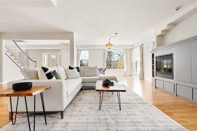 living room featuring stairway, a fireplace, light wood-type flooring, and baseboards