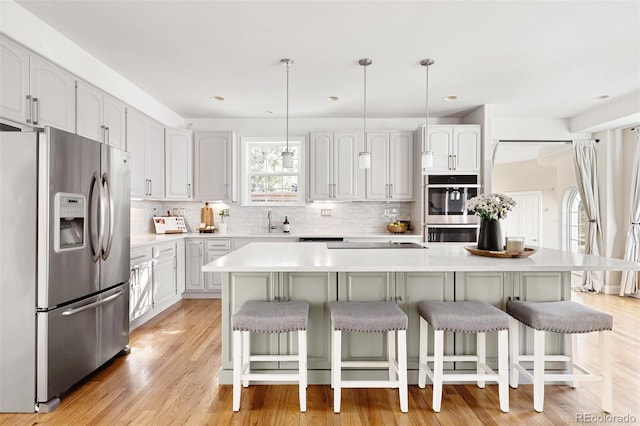 kitchen with tasteful backsplash, a kitchen bar, light countertops, light wood-style floors, and stainless steel appliances