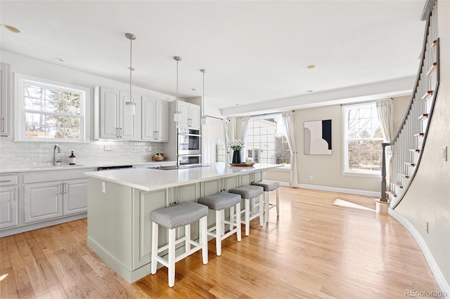 kitchen with light wood-type flooring, an island with sink, a sink, a kitchen breakfast bar, and tasteful backsplash