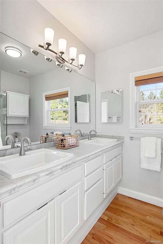 full bath featuring double vanity, wood finished floors, baseboards, and a sink