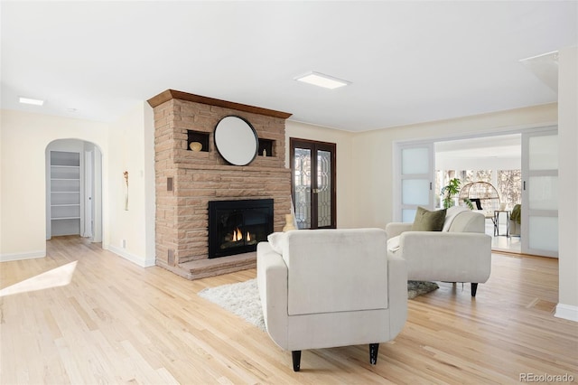 living area with light wood finished floors, a stone fireplace, arched walkways, and baseboards