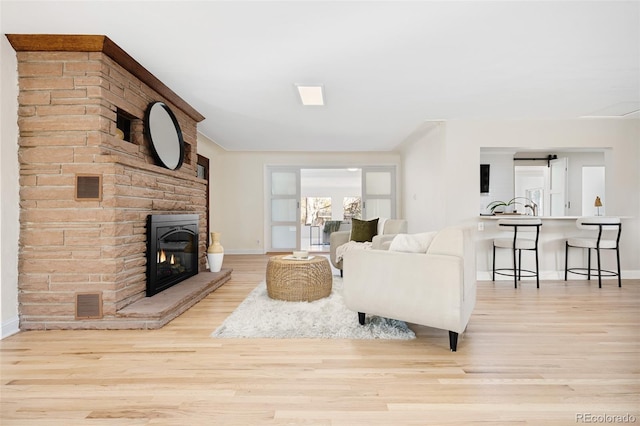 living room with visible vents, a brick fireplace, baseboards, and wood finished floors