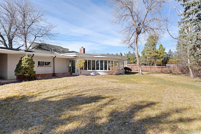 back of house with fence, a yard, a sunroom, a chimney, and brick siding