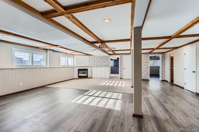 31142 County Road 18, Keenesburg, CO 80643 - unfurnished living room with wood finished floors, wainscoting, beamed ceiling, ceiling fan, and a glass covered fireplace