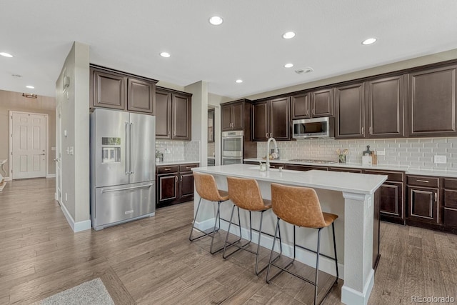 6738 Esmeralda Dr, Castle Rock, CO 80108 - kitchen featuring appliances with stainless steel finishes, a sink, dark brown cabinetry, light wood-style floors, and a center island with sink
