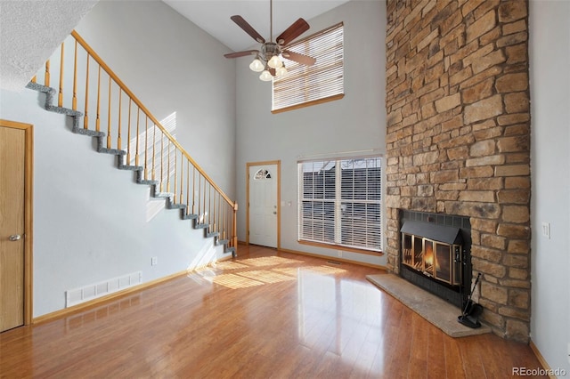 unfurnished living room featuring a high ceiling, ceiling fan, hardwood / wood-style floors, and a fireplace