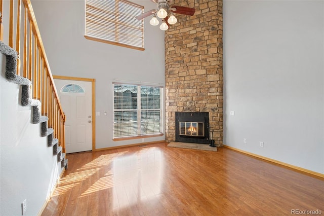 unfurnished living room with ceiling fan, a stone fireplace, light hardwood / wood-style floors, and a high ceiling