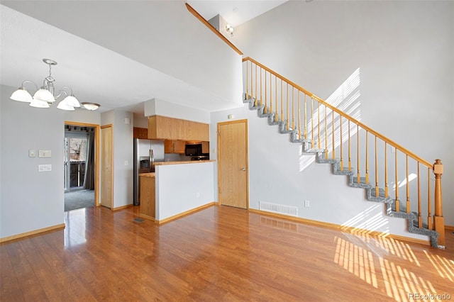 unfurnished living room with a notable chandelier, light hardwood / wood-style flooring, and a high ceiling