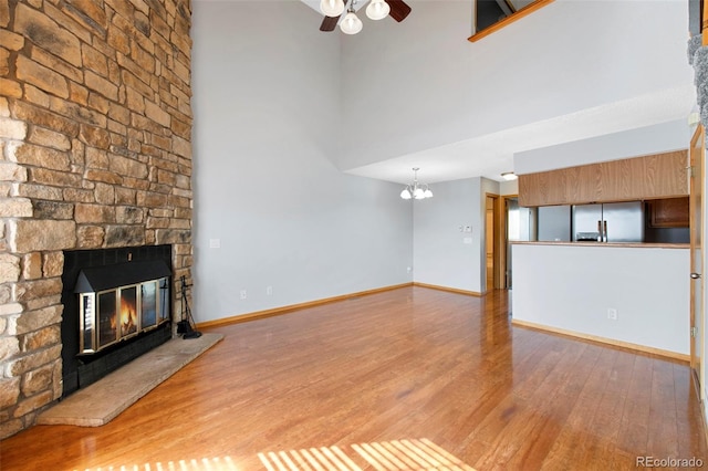 unfurnished living room featuring a fireplace, ceiling fan with notable chandelier, a high ceiling, and light wood-type flooring