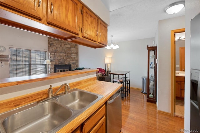 kitchen featuring a stone fireplace, sink, decorative light fixtures, a textured ceiling, and dishwasher