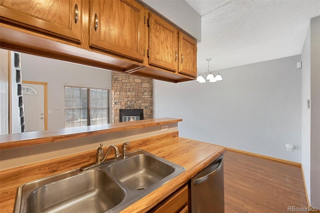 kitchen with hardwood / wood-style floors, sink, hanging light fixtures, stainless steel dishwasher, and a textured ceiling