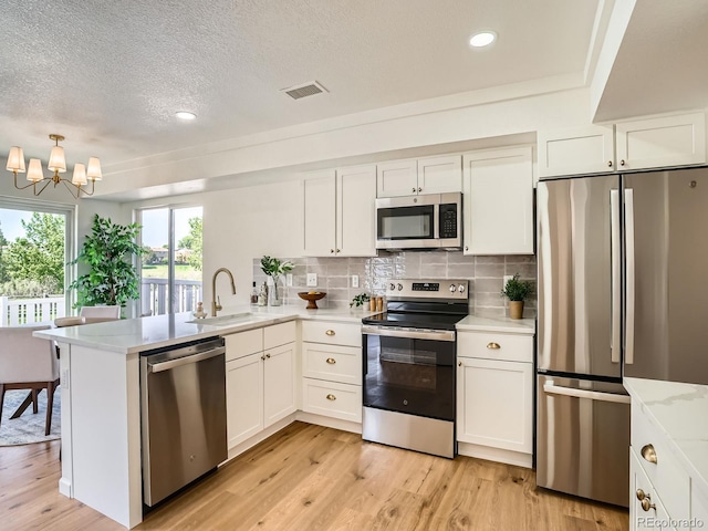 21472 E 46th Ave, Denver, CO 80249 - kitchen with appliances with stainless steel finishes, a sink, a peninsula, light wood finished floors, and white cabinets