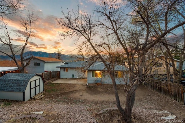 2121 Carmel Dr, Colorado Springs, CO 80910 - back of property at dusk with a shingled roof, a storage shed, a patio area, fence, and an outbuilding