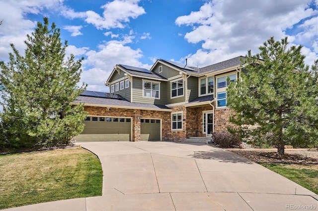 craftsman house with a front lawn, stone siding, an attached garage, driveway, and solar panels