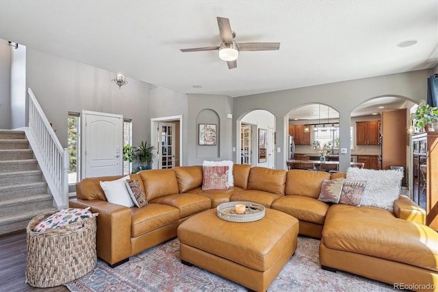 living area with arched walkways, a ceiling fan, stairs, and wood finished floors