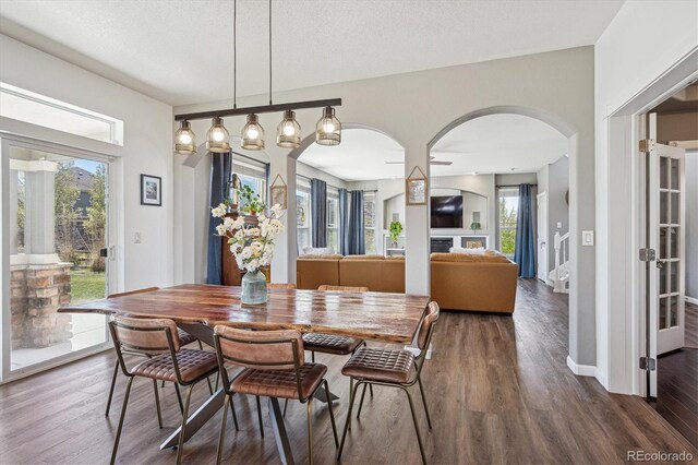 dining space with arched walkways, baseboards, and wood finished floors