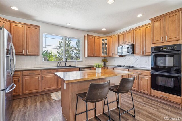 kitchen featuring dark wood-style flooring, a breakfast bar area, brown cabinets, a sink, and black appliances